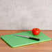 A San Jamar green cutting board with a tomato and a knife.