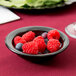 A Carlisle Dallas Ware black melamine fruit bowl filled with raspberries and blueberries.