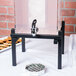 A Cal-Mil black metal base for a beverage dispenser with a faucet on a table.