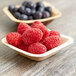 A  EcoChoice square palm leaf bowl filled with raspberries and blueberries on a table.