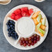 A EcoChoice compostable palm leaf deli tray with fruit and dip, carrots, and a variety of fruit on it.