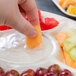 A person using an EcoChoice compostable palm leaf deli tray to dip fruit into a bowl of fruit.