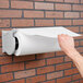 A person using a Bulman Deluxe paper dispenser on a brick wall.