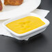 A Tuxton bright white rectangular china sauce bowl filled with yellow sauce on a white plate.