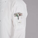 A person wearing a Mercer Culinary unisex white chef jacket with black piping and a phone in the pocket.