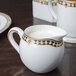 A white and gold Syracuse China creamer with a handle.