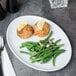 A Libbey Aluma White Porcelain coupe platter with meatballs and green beans with lemon slices on top.