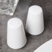 Two white Libbey porcelain salt shakers on a table.