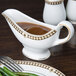 A Syracuse China Baroque bone china sauce boat with gravy on a plate.
