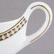A white bone china sauce boat with gold accents and a gold handle.