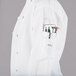 A white Mercer Culinary women's chef jacket with black piping and a pocket for a knife on the counter.