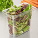 A Carlisle clear plastic food pan filled with salad greens and carrots.