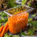 A Carlisle clear plastic food pan filled with shredded carrots on a table in a salad bar.