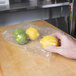 A hand holding a LK Packaging plastic bag with a lemon inside.