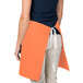 A woman wearing an orange Intedge waist apron with a pocket.