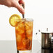 A hand using a Libbey stainless steel iced tea spoon to stir a glass of iced tea with a lemon slice.