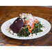 A plate of kale salad with beets, nuts, and vegetables on a 10 Strawberry Street Bistro porcelain dinner plate.