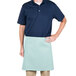 A man wearing a blue polo shirt and a sea green Intedge waist apron standing at a counter in a professional kitchen.
