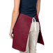 A woman wearing a burgundy Intedge waist apron with a pocket.
