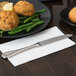 A Libbey stainless steel dinner knife on a white napkin next to a plate of food on a table.