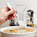 A hand holding a Libbey stainless steel soup spoon over a bowl of soup.