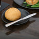 A black plate with a roll and a World Tableware Varese bread and butter knife on it.