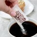 A hand holding a Sugar In The Raw organic white sugar packet over a cup of coffee.