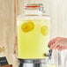 A hand pouring lemonade from an Acopa Country Glass Beverage Dispenser into a glass.