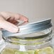 A hand using an Acopa mason jar beverage dispenser lid to open a jar of lemonade with lemon slices.