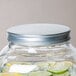 A white Acopa Mason jar beverage dispenser lid on a jar of water with lemons and limes.