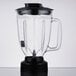 A clear Waring blender jar with a black lid and handle.