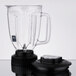 A clear copolyester Waring blender jar with a black lid and handle.
