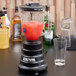 A Waring blender with a red liquid in it on a table.