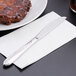 A Libbey stainless steel dinner knife on a napkin next to a plate of food.