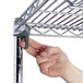 A hand holding a metal shelf with rubber casters for a Metro wire shelving unit.
