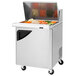A Turbo Air stainless steel refrigerated sandwich prep table with a door open and food on the trays.
