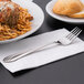 A Libbey stainless steel dinner fork on a napkin next to a plate of spaghetti and meatballs.