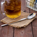 A Libbey stainless steel iced tea spoon in a glass of iced tea on a burlap napkin.