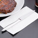 A Libbey Contempra stainless steel dinner knife on a napkin next to a plate of ribs.