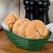 A green Carlisle WeaveWear serving basket with rolls on a table.