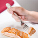 A person holding a Libbey Geneva stainless steel fish fork over a piece of food.