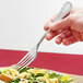 A hand holding a Libbey stainless steel dinner fork over a plate of salad.