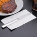 A Libbey stainless steel dinner knife on a napkin next to a plate of meat and rice.