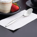 A Libbey stainless steel dessert spoon on a white napkin next to a cake.