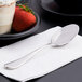 A Reserve by Libbey stainless steel dessert spoon on a napkin next to a bowl of strawberries.