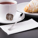 A cup of tea with a brown tag and a Libbey stainless steel demitasse spoon on a plate with a pastry.