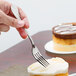 A Libbey stainless steel dessert fork being used to cut a cake.