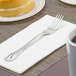 A Libbey stainless steel dessert fork on a napkin next to a cake.