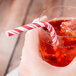 A hand holding a glass of red liquid with a Creative Converting red and white striped paper straw.