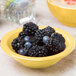 A close up of a Libbey saffron porcelain fruit bowl filled with blackberries and blueberries.